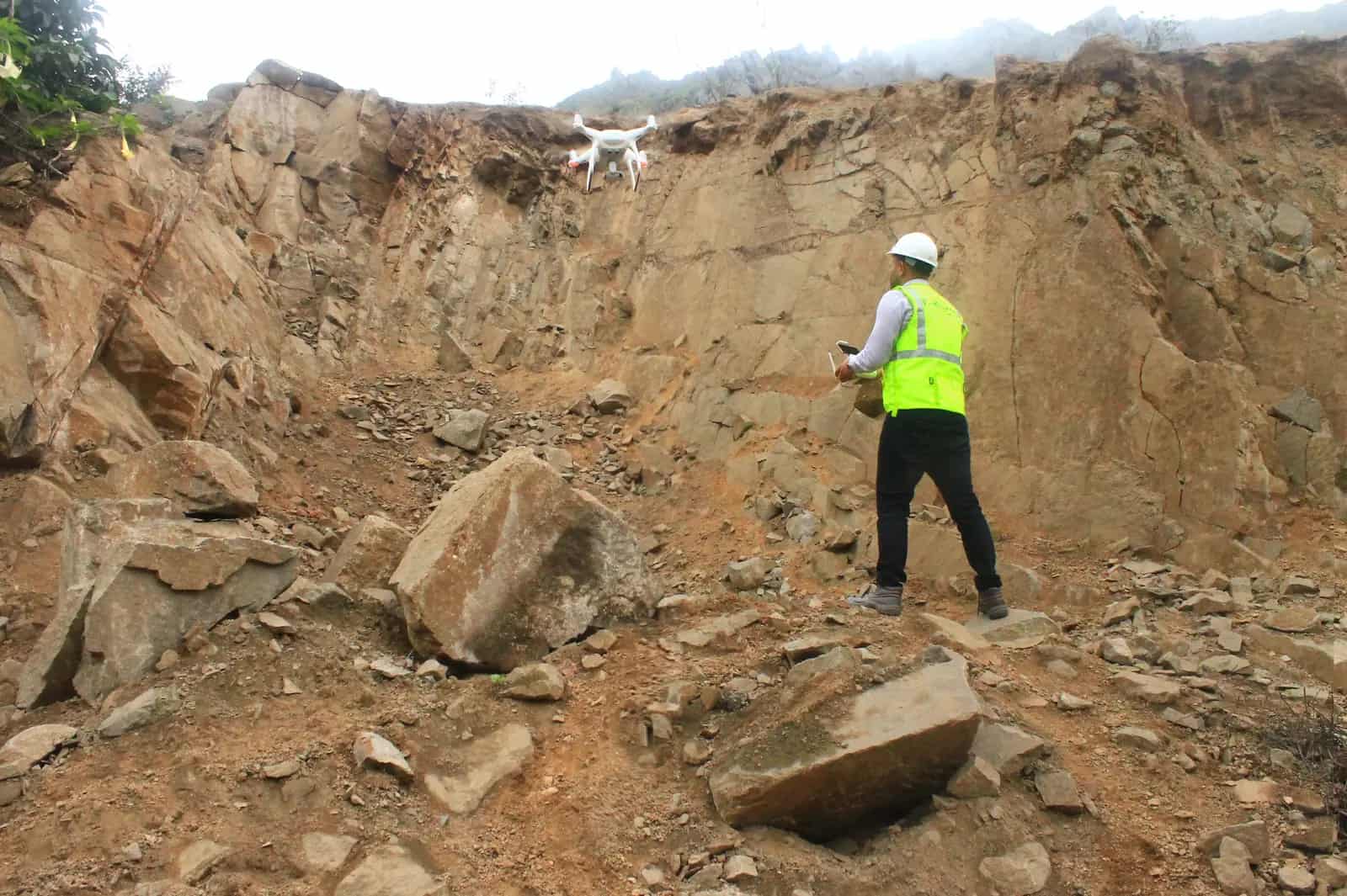 Ingeniero inspeccionando un talud rocoso mientras un drone sobrevuela la zona