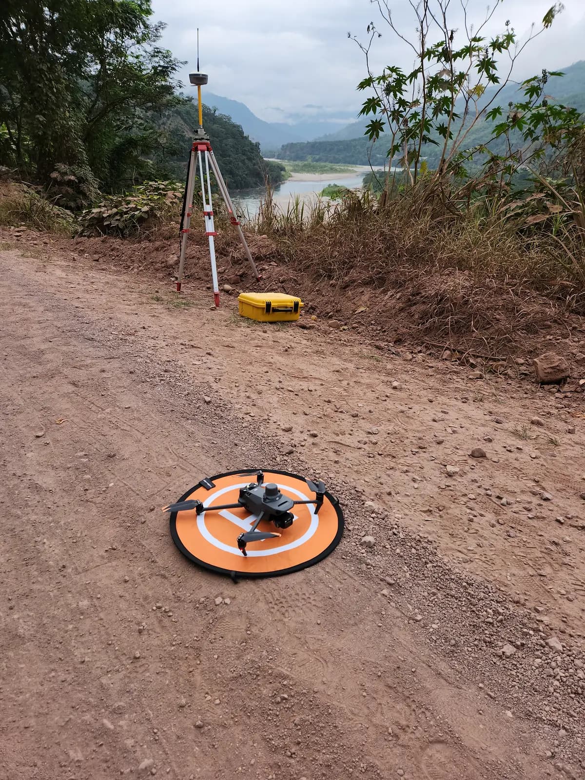 Drone Mavic 3 Enterprise en su plataforma junto a la base GNSS, frente a un valle de selva alta