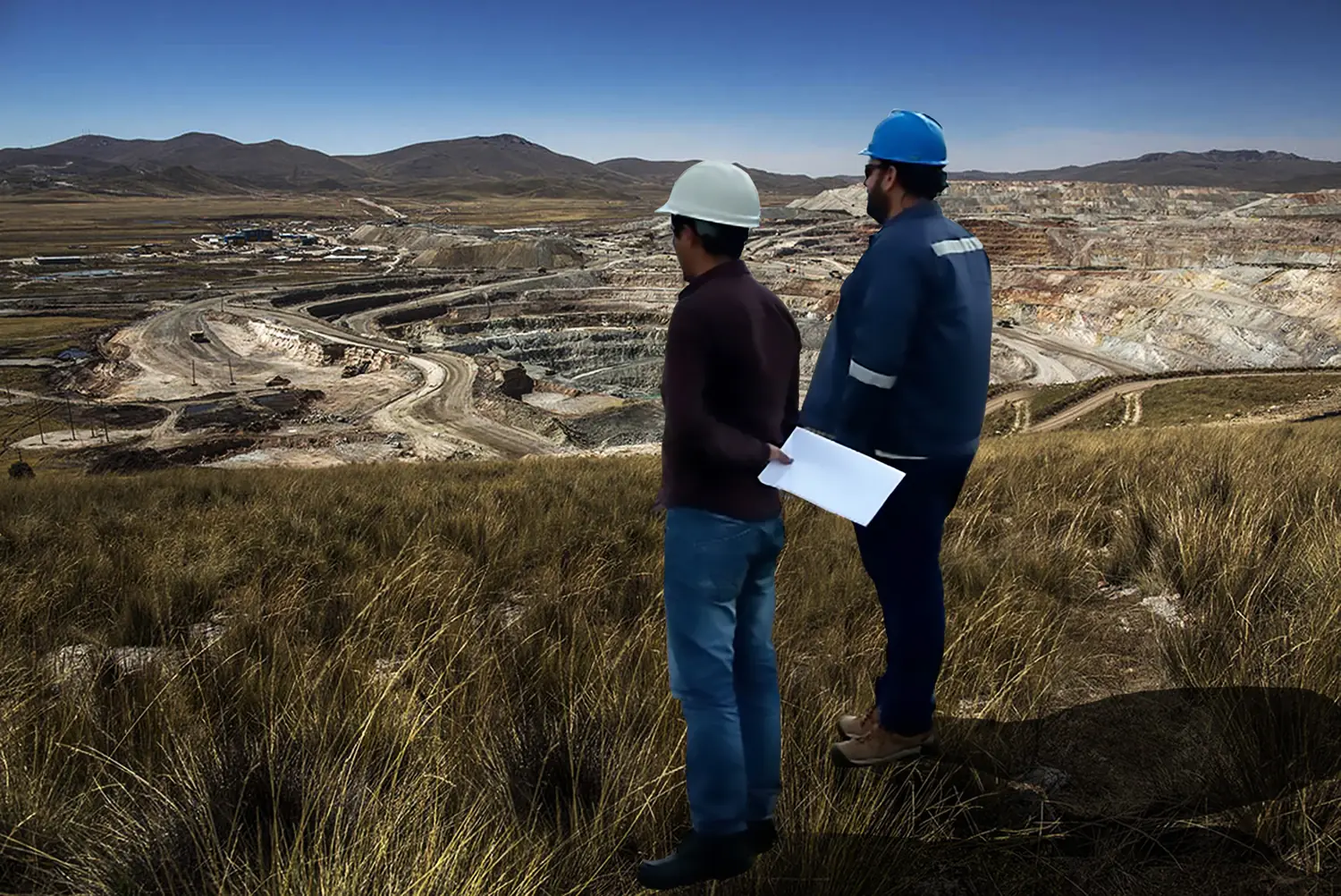 Dos ingenieros analizando planos en campo frente a un área de operaciones