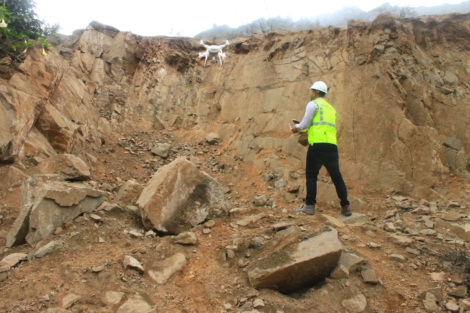 Ingeniero inspeccionando un talud rocoso mientras un drone sobrevuela la zona